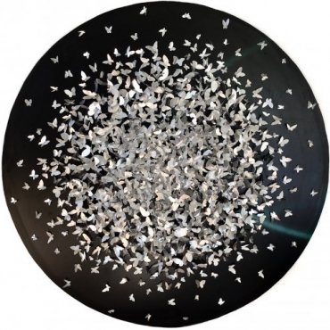 Hand-cut aluminium sheets in various butterfly shapes, glued together forming a circular shape on a black background.