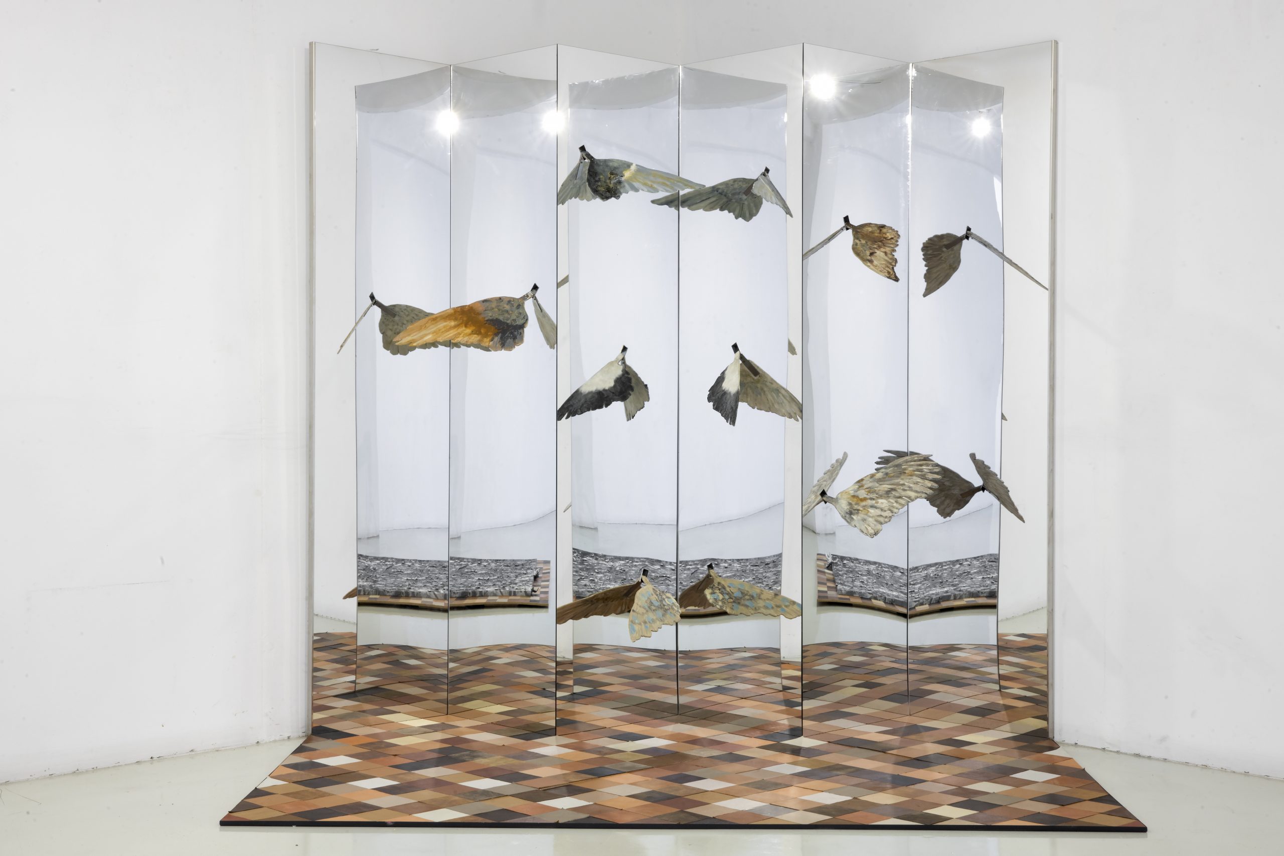 Mirrors at right angles with bird wings at various poisitons on them. A geometric flool with earth-tone leathers