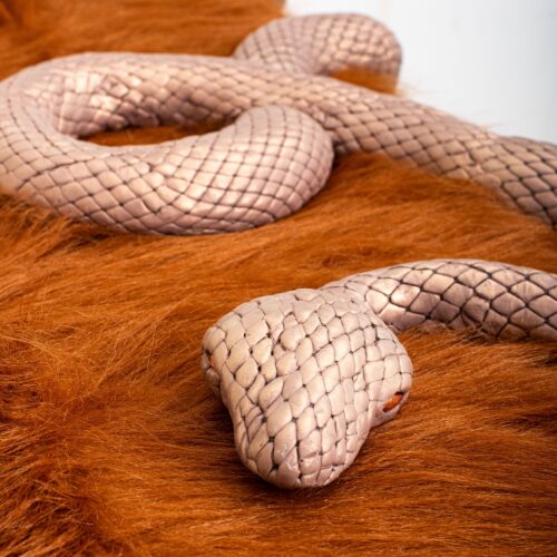 Close-up of beige braided snake-skin cords resting on orange-brown fur backdrop.