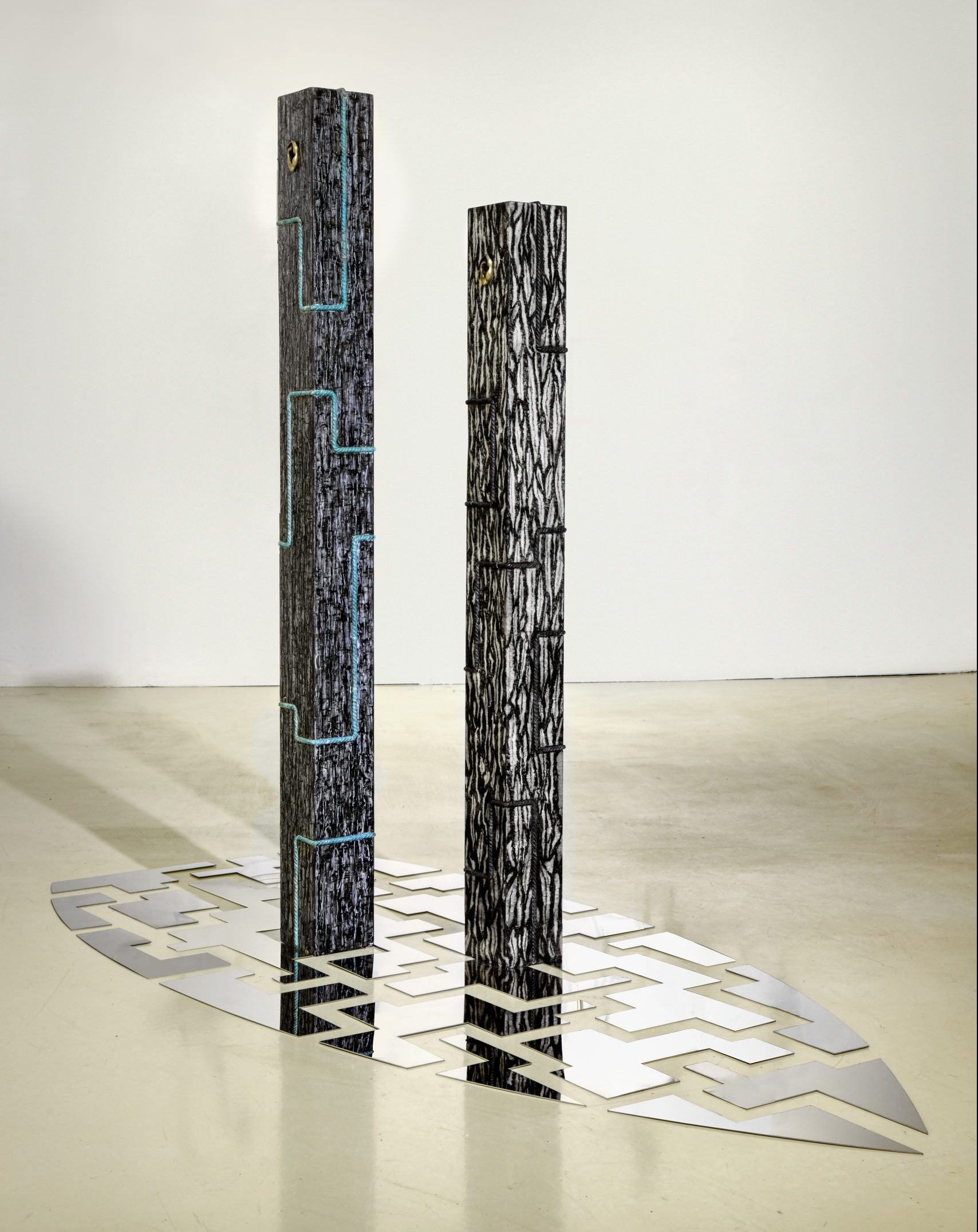floor art installation with geometric patterns and two wooden coloumns with bronze cord
