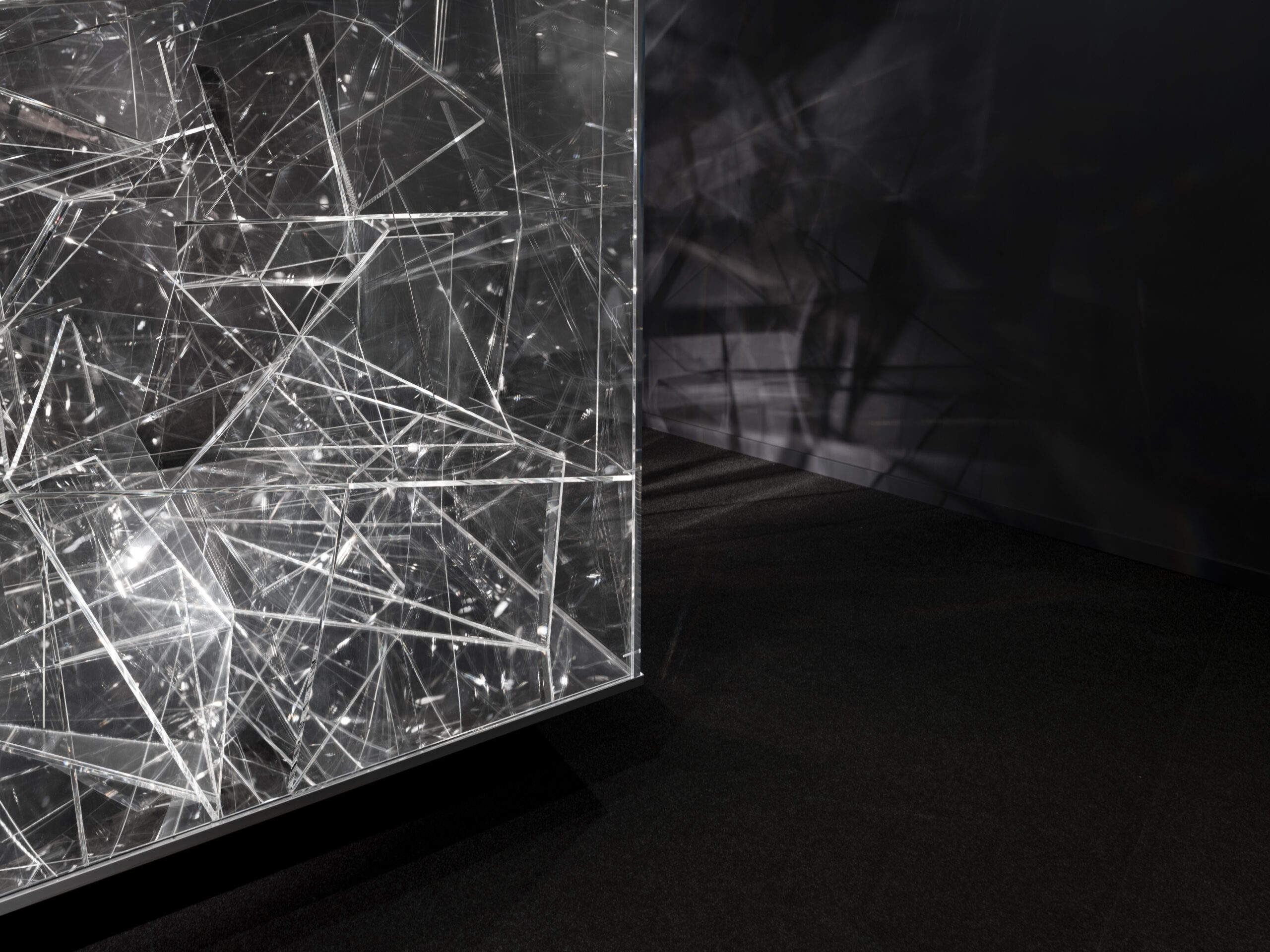 Abstract installation of clear glass panels with intersecting shards reflecting light in a dark room