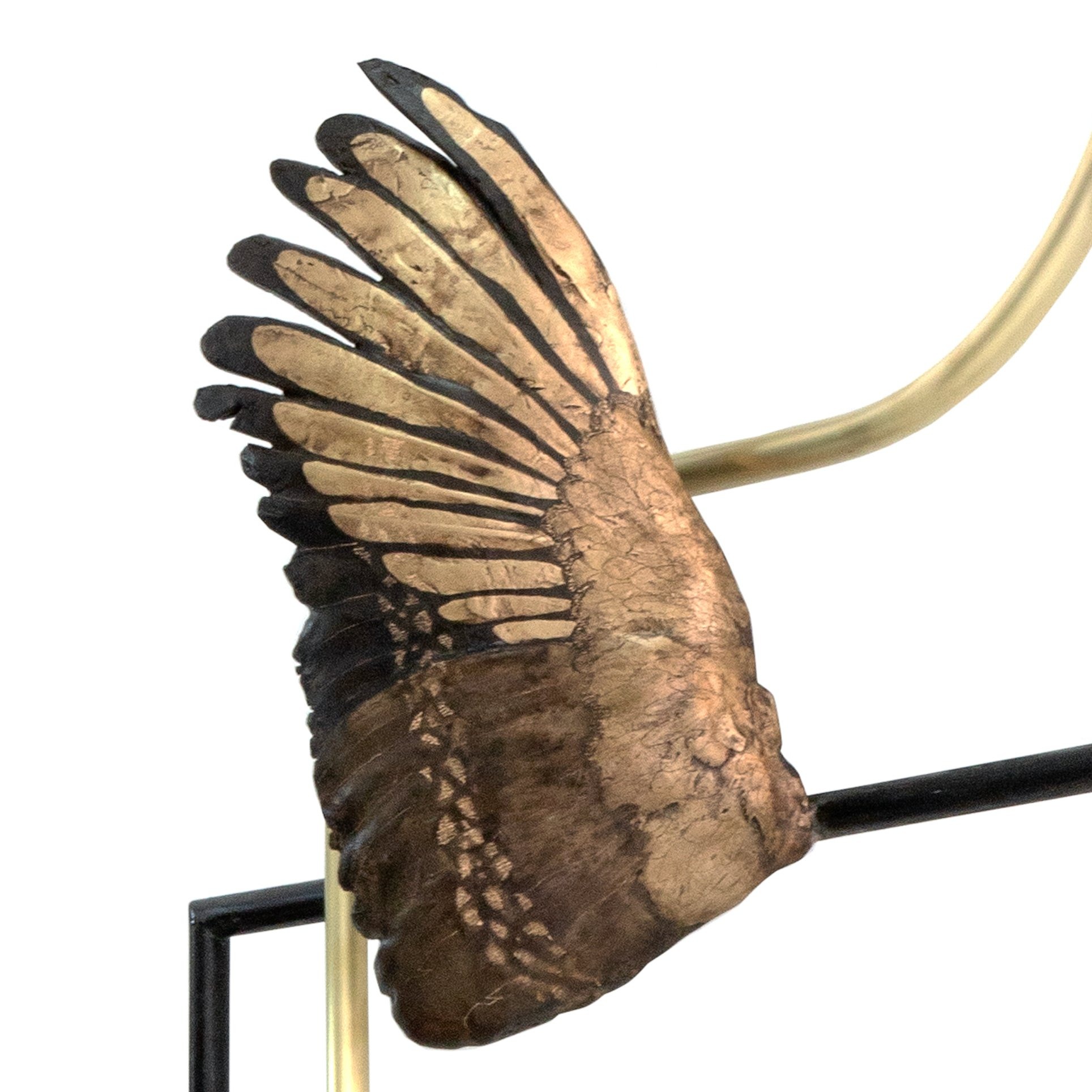 Bronze bird wing sculpture attached to a black metal railing, close-up of detailed feathers.